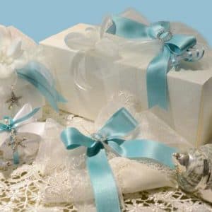 Confezioni regalo eleganti con nastri azzurri, decorazioni in argento e charms artigianali su fondo in pizzo bianco.