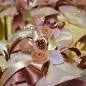 Composizioni artigianali con nastri crema e oro, rose in tessuto e perle decorative per confezioni regalo eleganti.