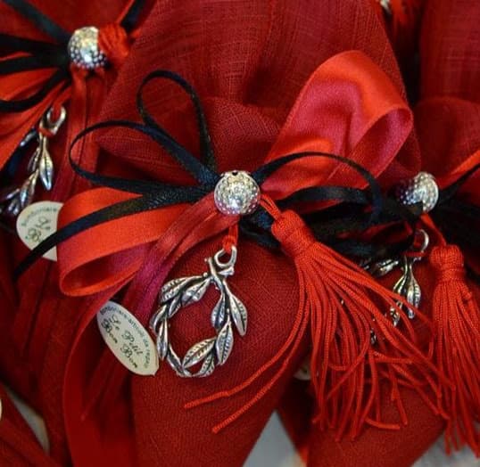 Sacchetti rossi artigianali con nastri decorativi, charms argentati e dettagli personalizzati per bomboniere di laurea.