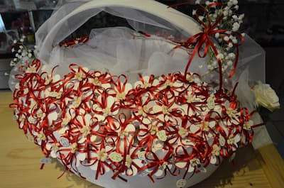 Cesto decorativo con sacchettini bomboniera per laurea, fiocchi rossi in raso, fiori bianchi e tulle su base in tessuto bianco.