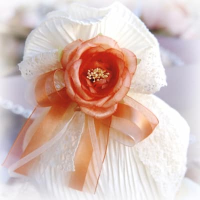 Bomboniera artigianale con fiore pesca, tessuto plissettato bianco, dettagli in pizzo e nastro in organza, ideale per matrimonio o evento elegante.