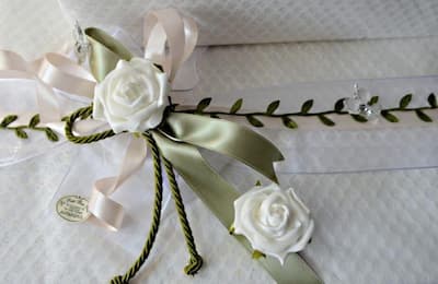 omboniera artigianale con rose bianche, nastri rosa e verde oliva, cordoncino decorativo e farfalla trasparente su base in tessuto bianco