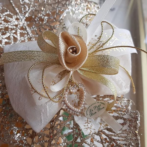 Elegante bomboniera artigianale con fiocco crema e dettagli dorati, decorata con perle e nastro, creazione esclusiva di Veronica Belluco per Alfafoto Le Petit Bon Bon.