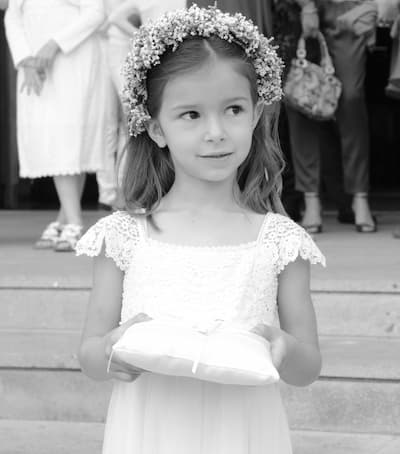 damigella vestita di bianco con corona floreale e cuscino cerimoniale, in un contesto elegante e formale