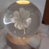 Sfera di cristallo luminosa con incisione 3D quadrifoglio e base circolare in legno.