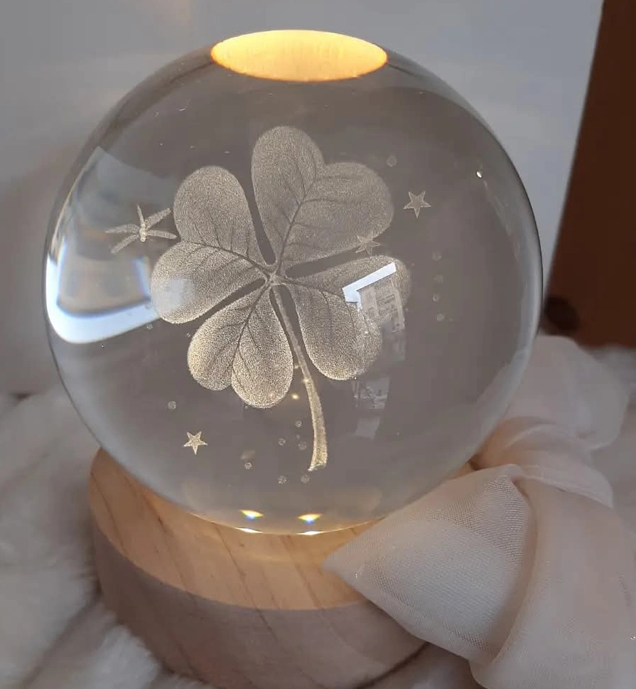 Sfera di cristallo luminosa con incisione 3D quadrifoglio e base circolare in legno.