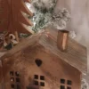 Lanterna portacandele in metallo color bronzo a forma di casa con tetto a tegole e comignolo. Presenta ritagli quadrati per le finestre e un piccolo cuore intagliato sul davanti.