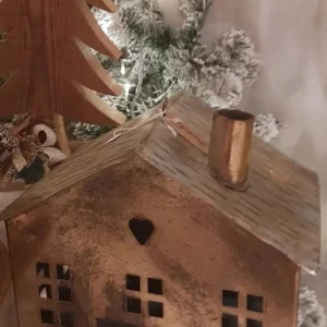 Lanterna portacandele in metallo color bronzo a forma di casa con tetto a tegole e comignolo. Presenta ritagli quadrati per le finestre e un piccolo cuore intagliato sul davanti.