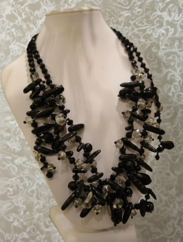 Collana multifilo con pietre nere lucide e cristalli trasparenti su manichino bianco, sfondo decorato