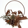 Decorazione natalizia in metallo marrone a forma di cerchio con silhouette di tre uccellini su un ramo. Ornamento arricchito da pigne, rami di pino e fiocco rustico color bronzo.