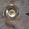 Globo di vetro trasparente con incisione 3D laser del Piccolo Principe su un pianeta con anello e stelle, poggiato su base LED in legno.