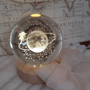 Globo di vetro trasparente con incisione 3D laser del Piccolo Principe su un pianeta con anello e stelle, poggiato su base LED in legno.