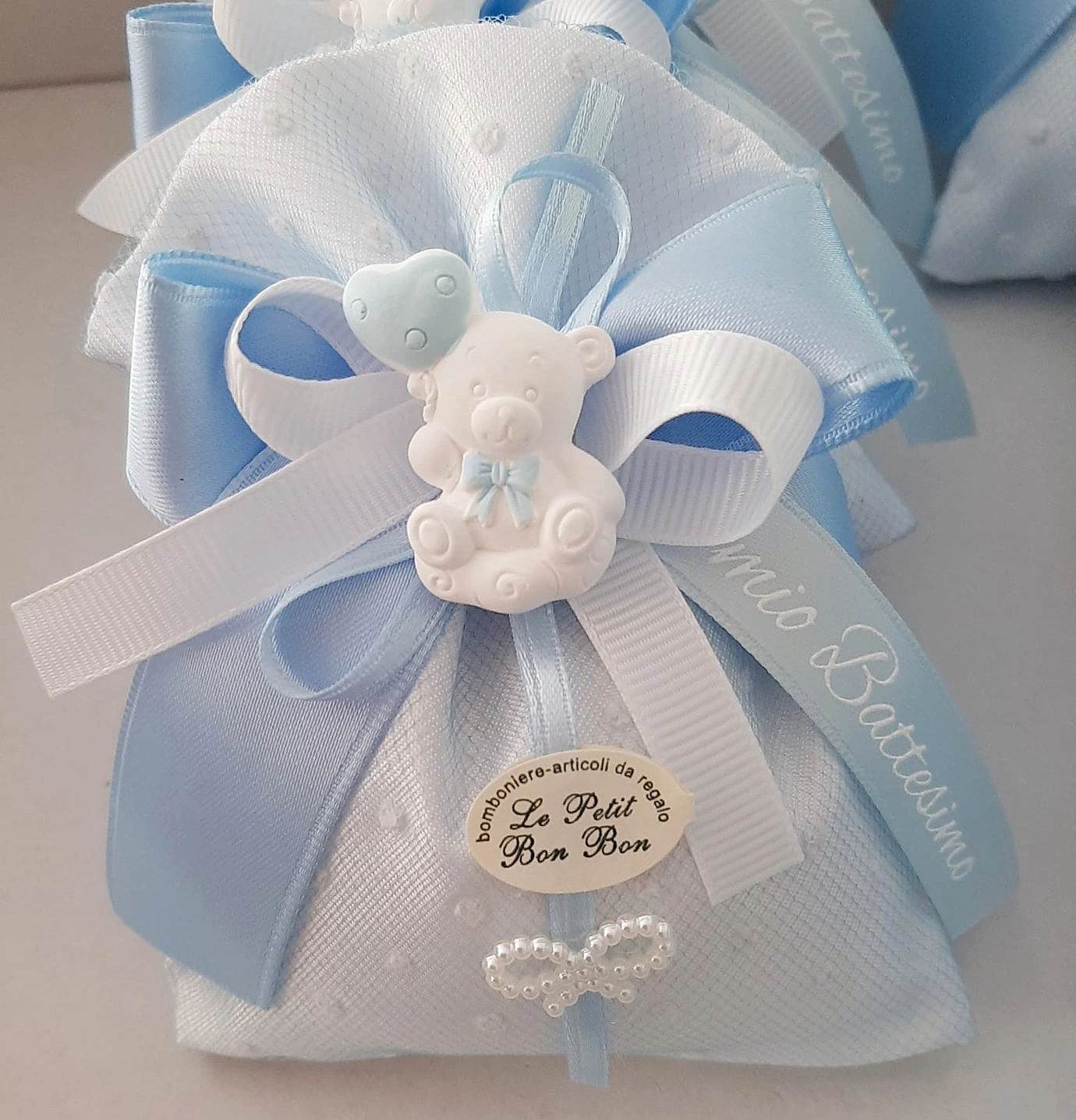 Sacchettino bomboniera battesimo in tulle bianco ricamato con fiocco azzurro e orsetto in gesso con palloncino. Etichetta "Le Petit Bon Bon"